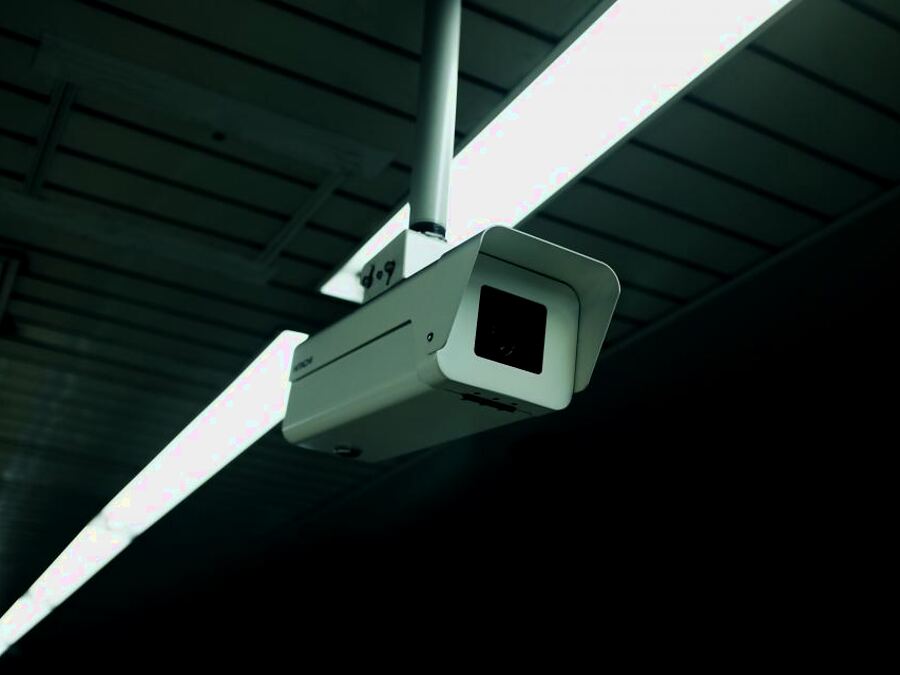 Close-up of a bullet CCTV camera on a ceiling bracket beside a fluorescent light